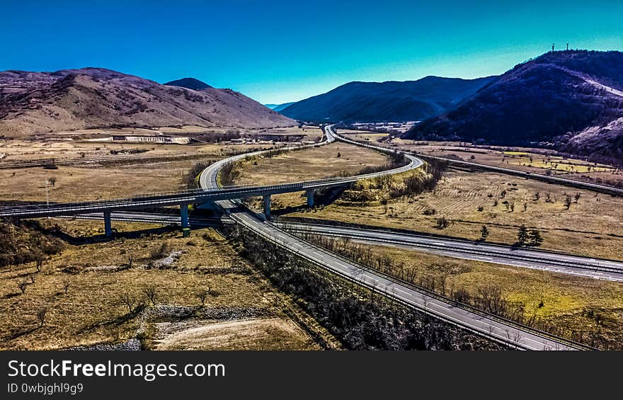 Aerial view of a highway intersection in a rural and mountainous area. We are in the daytime and the road is not very busy. Aerial view of a highway intersection in a rural and mountainous area. We are in the daytime and the road is not very busy