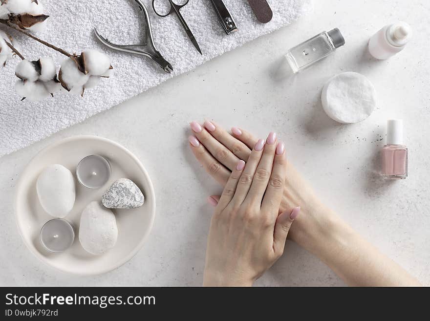 Woman`s hands with delicate pink manicure on the background of manicure tools. nails salon and spa. White concrete background, top view