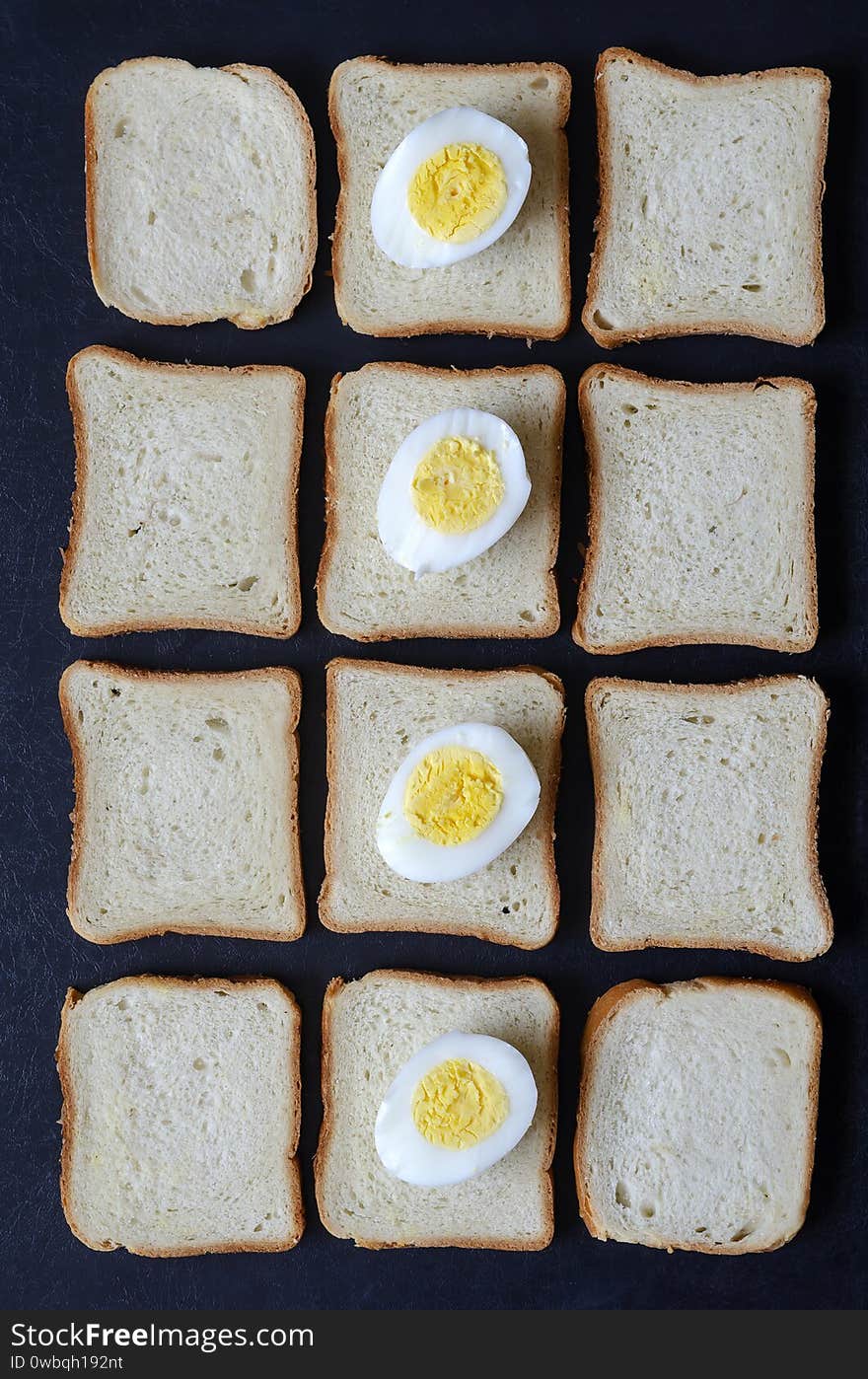 Food industry background. Boiled chicken eggs and toast bread. Vertical line of half-cut boiled chicken eggs. Template for the menu. View from above. Place for text