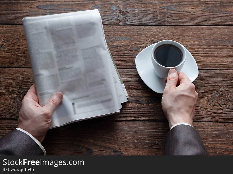 Top view on male hands holding a German newspaper and a cup of black coffee. Reading the news in the morning.  Finance, business. Place for text.