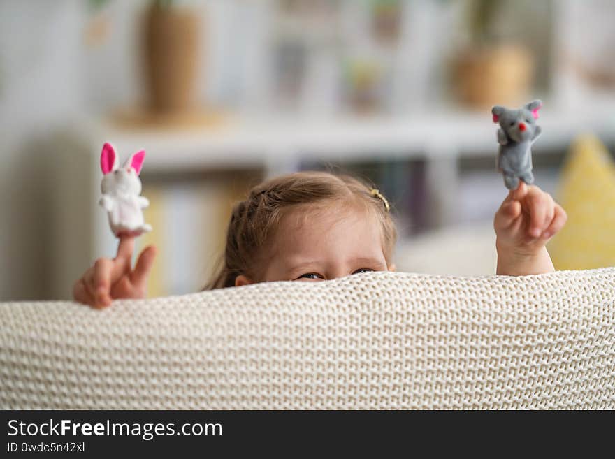 Funny little girl playing in theater. Finger puppets are put on the child`s hands. child laugh laughs, looks out from behind shelter and shows performance. Development of imagination and creativity. Funny little girl playing in theater. Finger puppets are put on the child`s hands. child laugh laughs, looks out from behind shelter and shows performance. Development of imagination and creativity