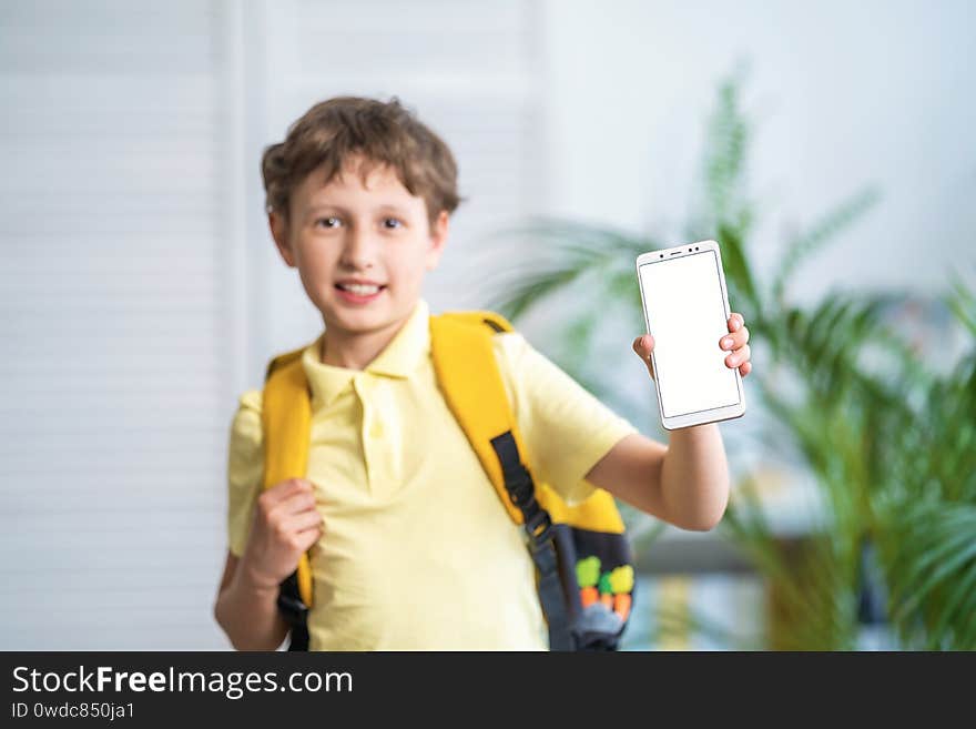 Cheerful schoolboy with a backpack shows white mobile phone screen. E-learning