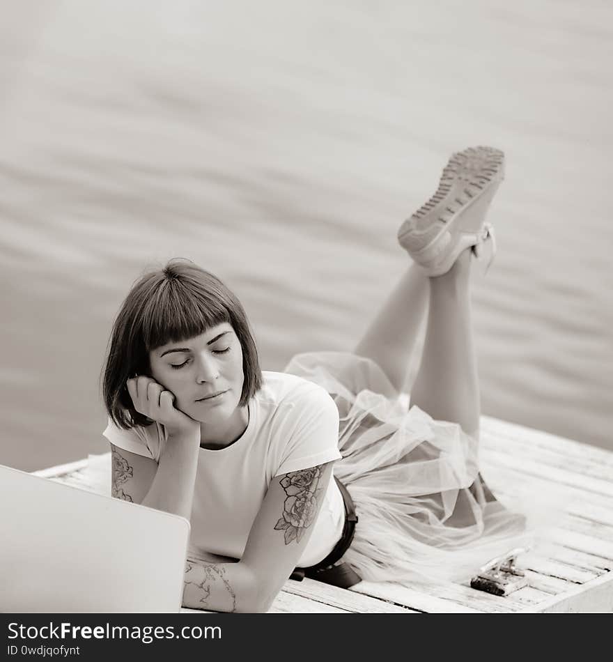 Content writer thinking text on laptop while lying on pier with closed eyes. Content writer thinking text on laptop while lying on pier with closed eyes