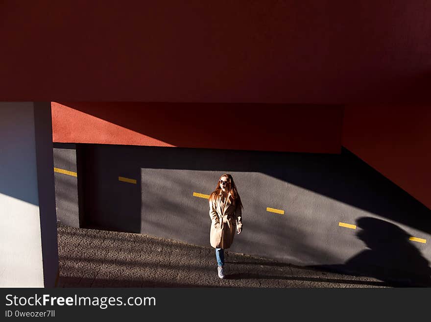 Fashion red hair woman in long beige coat and sunglasses walking on urban street