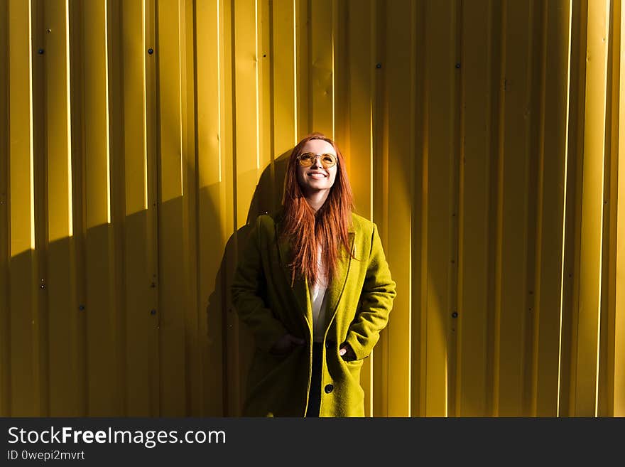 Happy red hair girl standing against yellow wall and looking up. Copy space