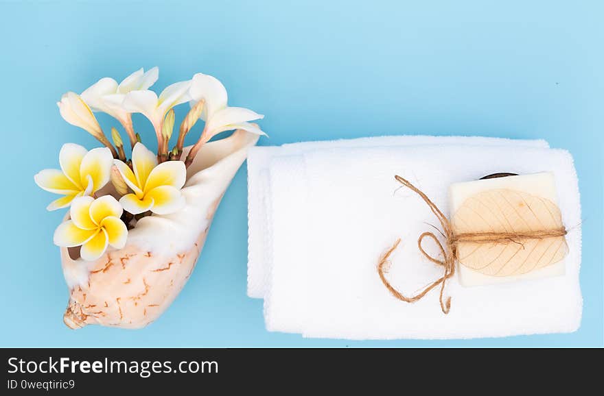 White towel and beautiful frangipal or plumeria spa flower  in sea shell vase and coconut soap on blue background, top view