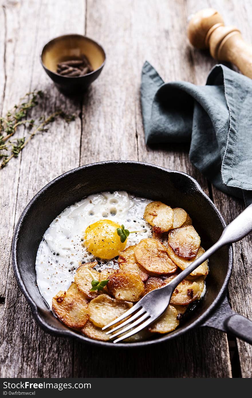 Fried Eggs and Potatoes in cast iron skillet on rustic wooden table. Skillet Breakfast. Selective focus