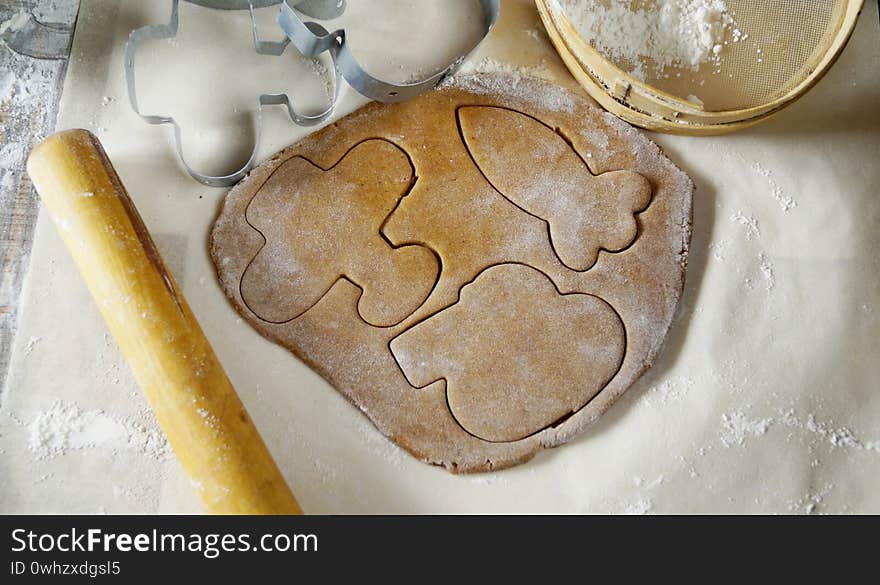 Gingerbread dough is rolled on the table. Figures are cut out of it with moulds. The table is suppaned with flour