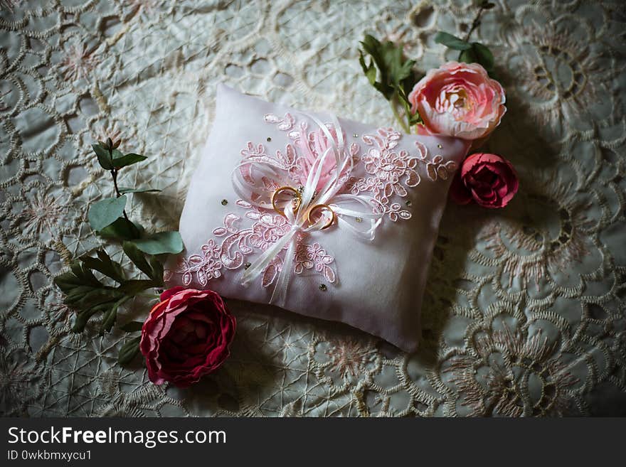 A couple of wedding rings on a small white cushion decorated with pink flowers. A couple of wedding rings on a small white cushion decorated with pink flowers.