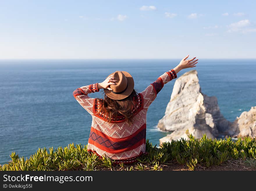 Closeup back view of woman in travel clothes and hat sitting and looking at blue ocean and sky. Travel concept photo