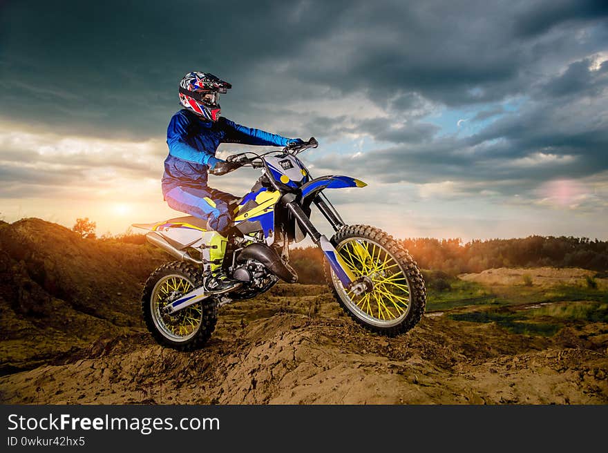 Side View Footage of the Professional Motorcycle Rider Driving on the mountains and Further Down the Off-Road Track. It`s Sunset and Track is Covered with Smoke Mist.