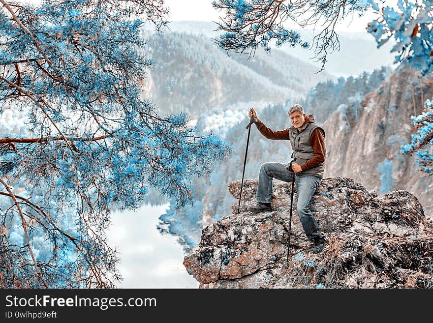 A man with Scandinavian sticks sits on top of a mountain