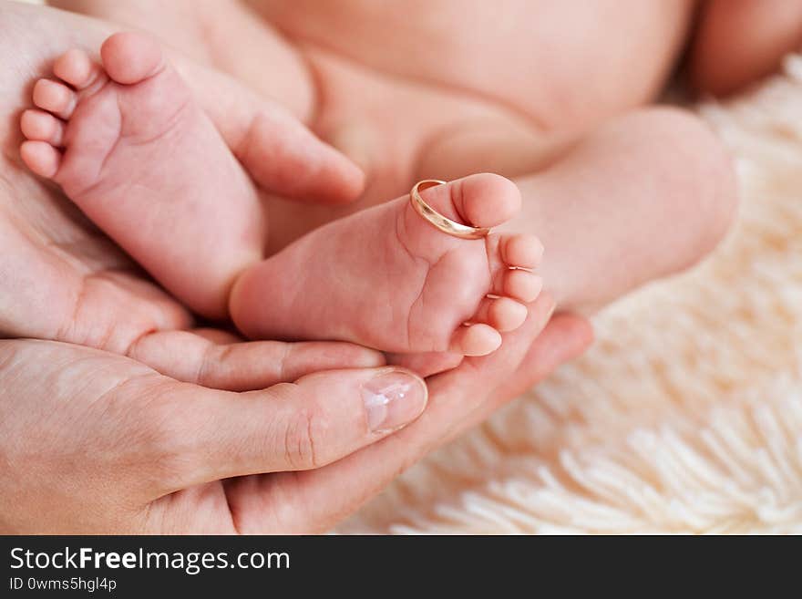 Mother hold feets with gold ring of newborn baby. day