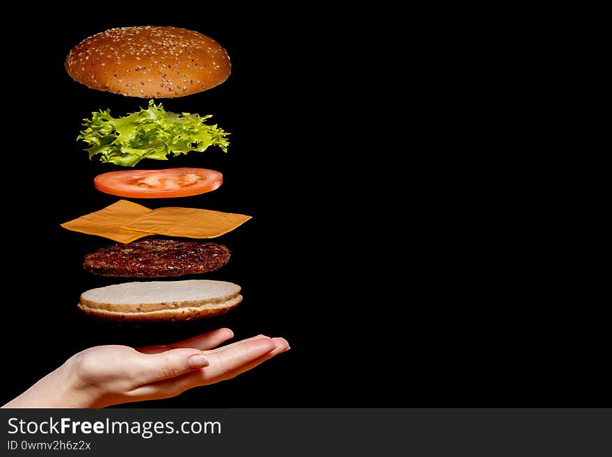 Flying ingredients burger or cheeseburger on a small wooden cutting board isolated on a dark background. Burger floating in the