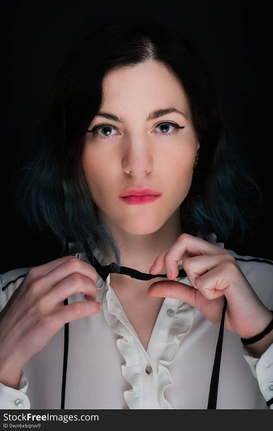 Portrait of a young caucasian woman with serious face expression and black and blue gradient colored hair. Dark background, white blouse. Portrait of a young caucasian woman with serious face expression and black and blue gradient colored hair. Dark background, white blouse