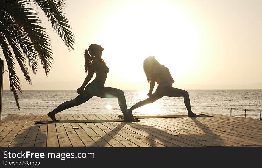 Silhouette of two women practice warrior yoga posture at seaside in sunshine