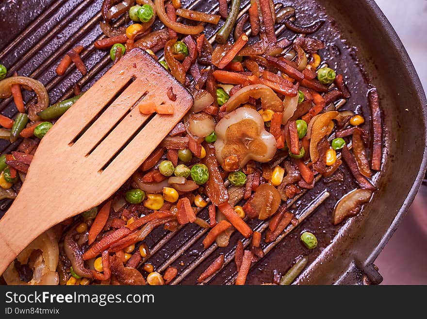 Grilled vegetables lie on a ribbed frying pan together with a wooden spoon