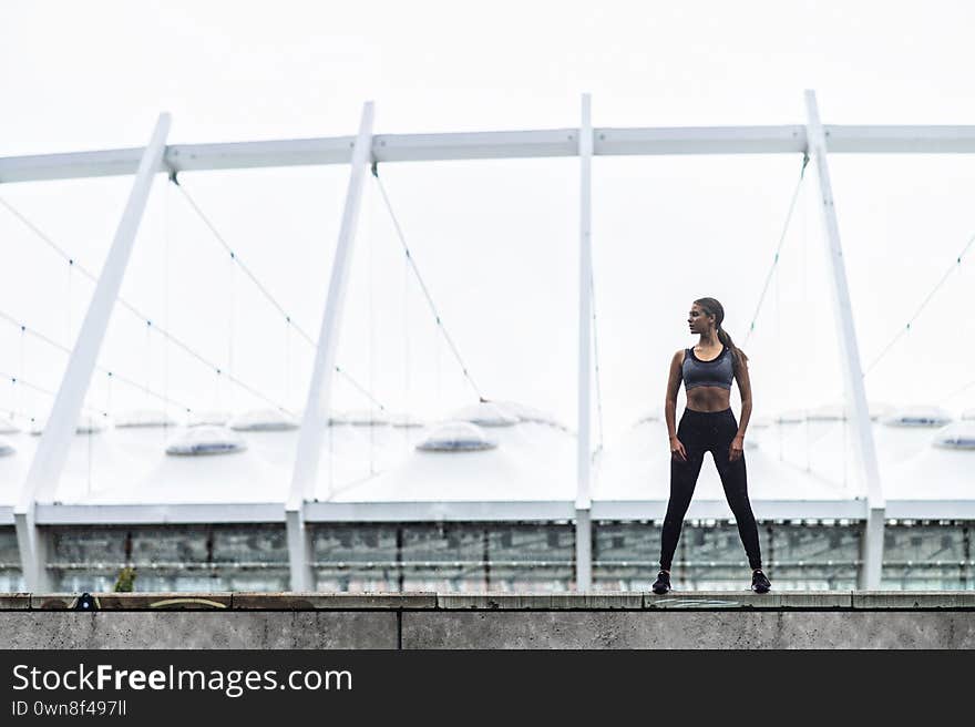 Keep your body in good shape. Slender young woman in sportswear stands in confident pose, a stadium on background. Keep your body in good shape. Slender young woman in sportswear stands in confident pose, a stadium on background