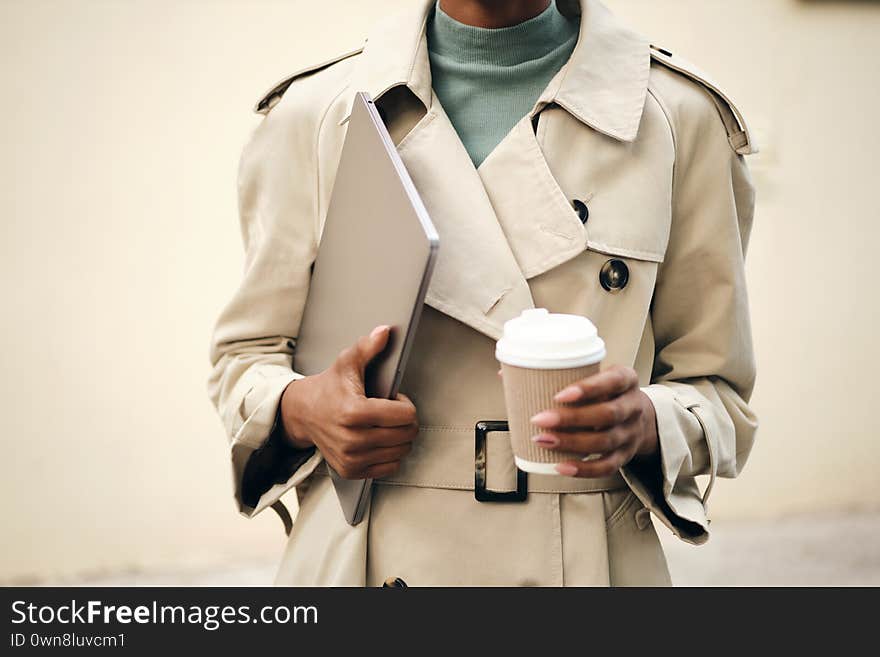 Close up casual woman in stylish trench coat with laptop and coffee to go outdoor