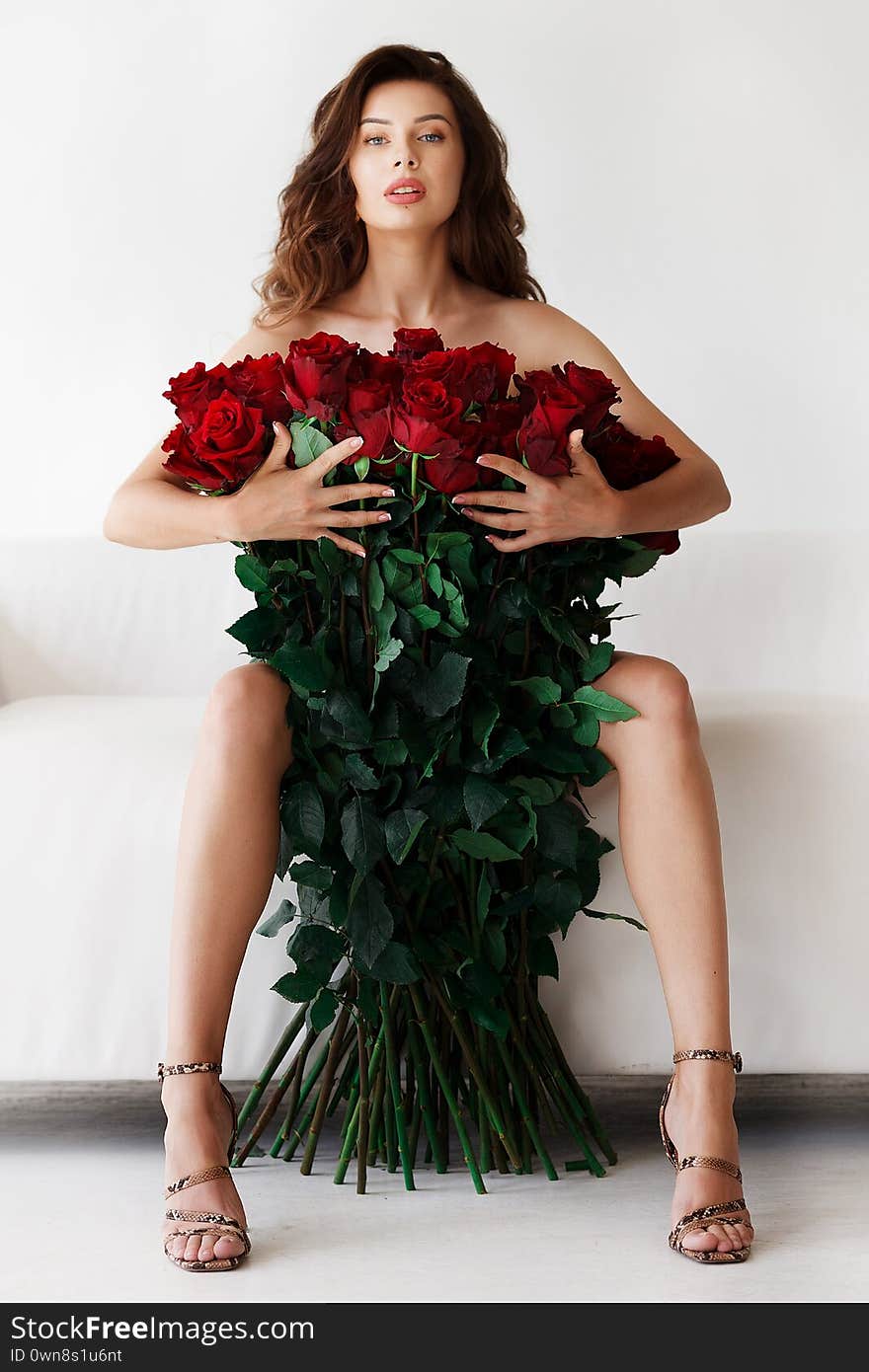 A beautiful naked girl is sitting on a luxurious white sofa, and holding a bouquet of big red roses in front of her. A beautiful naked girl is sitting on a luxurious white sofa, and holding a bouquet of big red roses in front of her.