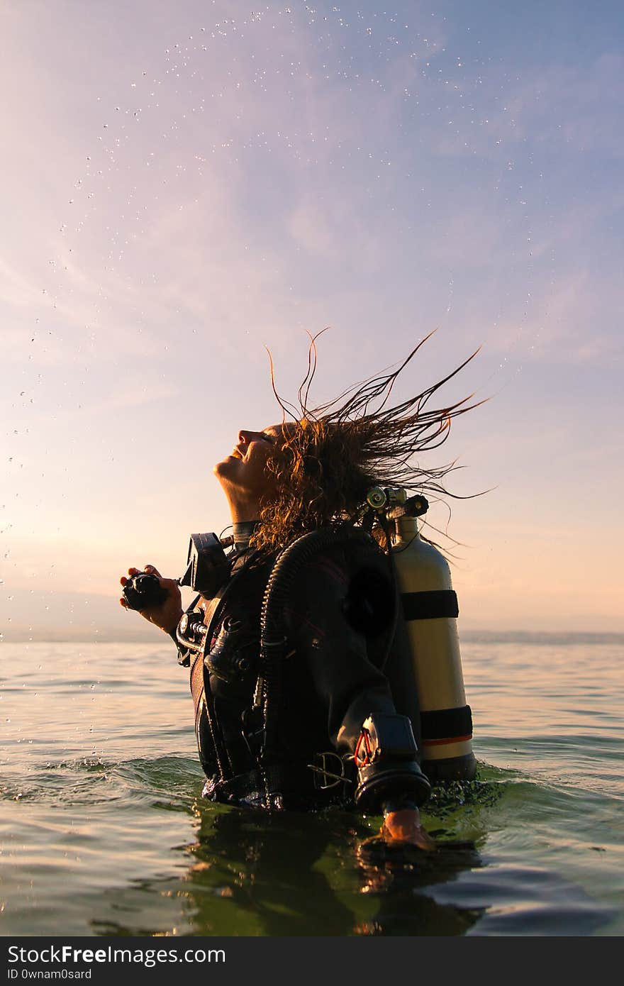 Female Scuba Dive Instructor Wearing a Dry Suit, a Twin Tank and Holding Fins Flipping Wet Hair in the Air