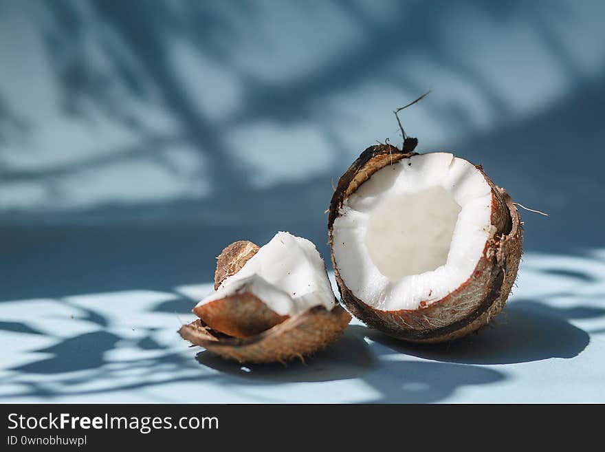 Half a coconut and pieces of coconut on a blue background. The shadow of the leaves.