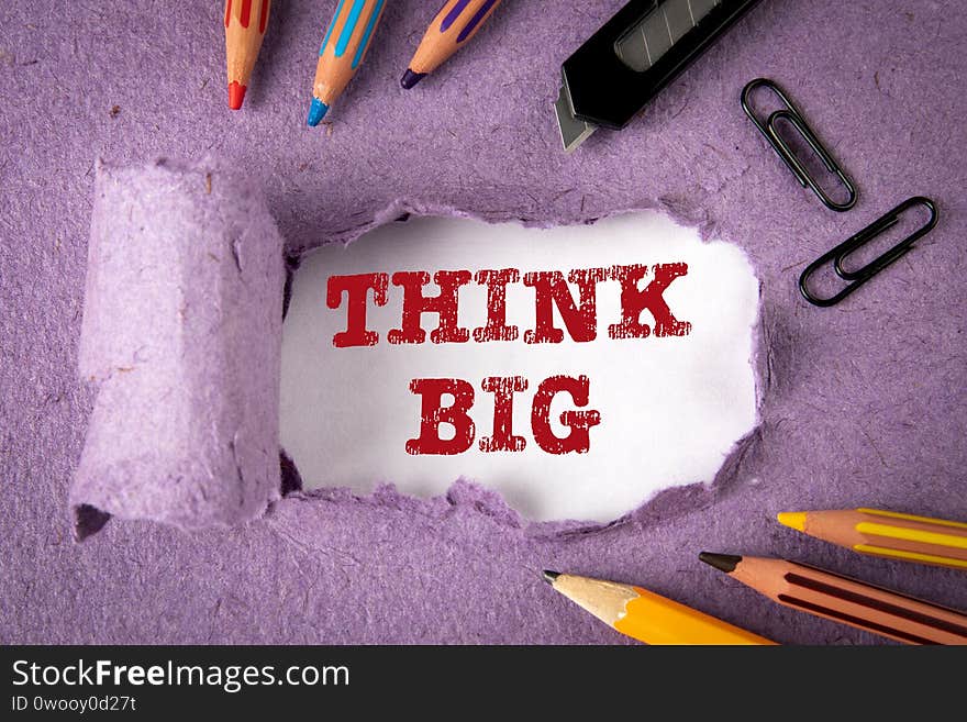 THINK BIG concept. Text under torn paper. Pencils and office supplies