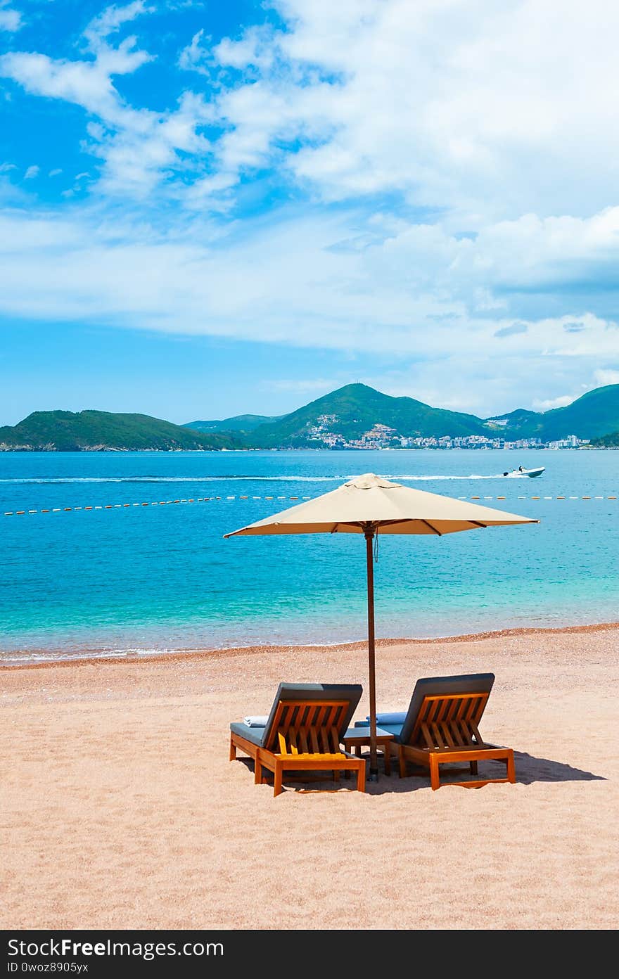 Two chaise lounges with umbrella on the beach. Beautiful beach with white sand and blue sea near Budva, Montenegro. Two chaise lounges with umbrella on the beach. Beautiful beach with white sand and blue sea near Budva, Montenegro