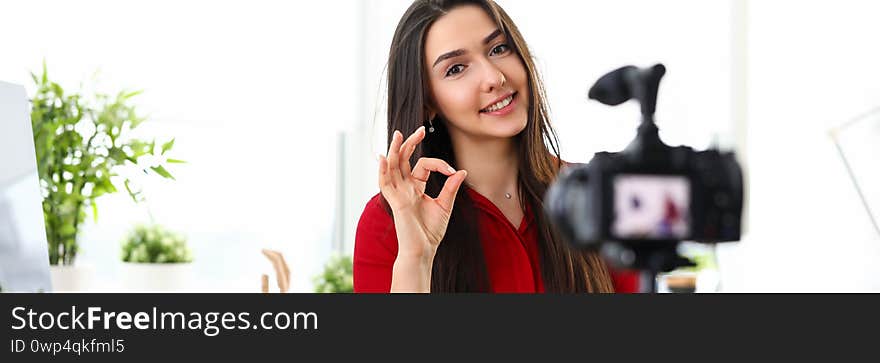 Portrait of beautiful smiling woman recording video-blog on video camera. Cheerful blogger showing ok sign with fingers. Blogging and creation concept. Portrait of beautiful smiling woman recording video-blog on video camera. Cheerful blogger showing ok sign with fingers. Blogging and creation concept