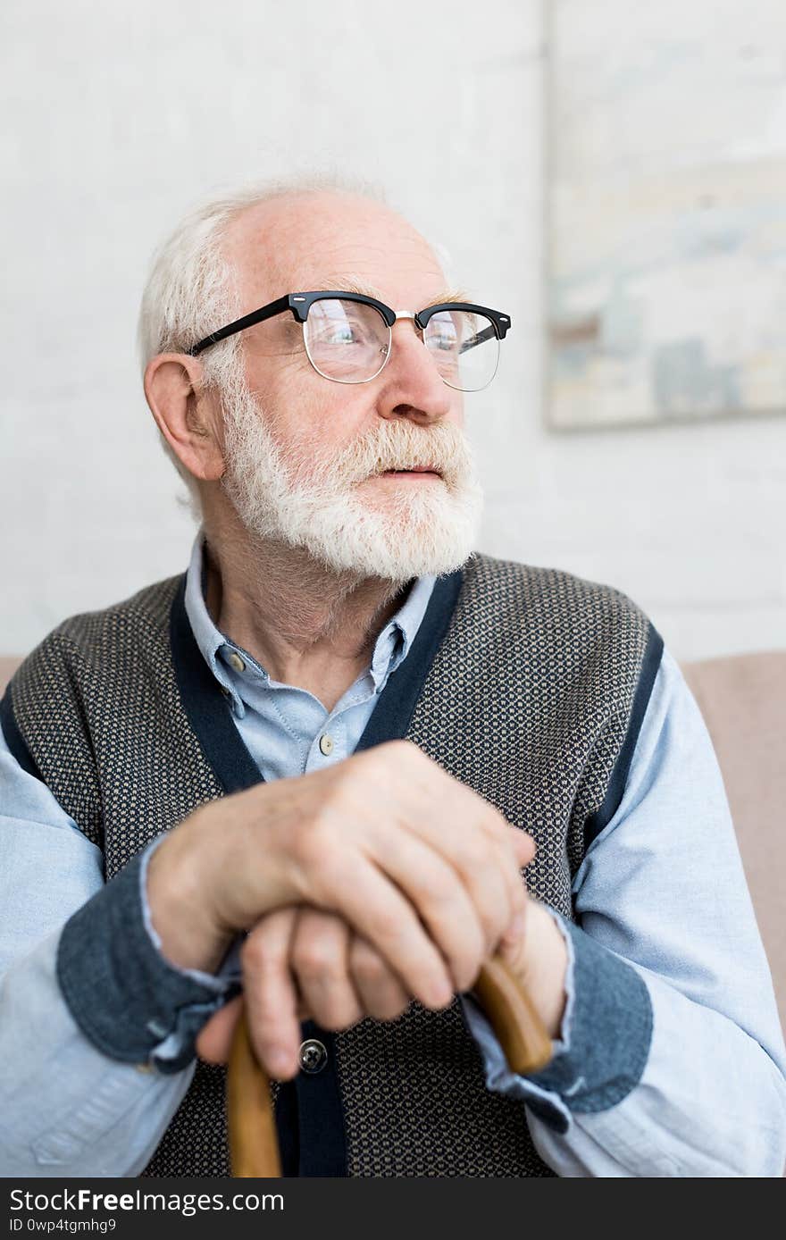 Calm and sad senior man with walking stick looking away, sitting