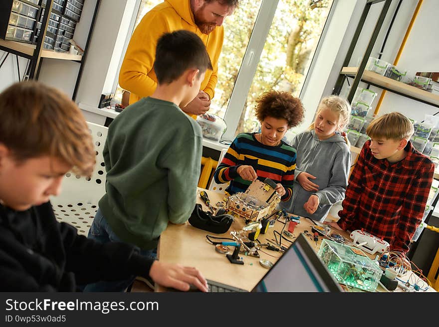 Young technicians building a robot vehicle together with a male teacher at a stem robotics class. Inventions and creativity for kids. Tinkering, educational activities concept. Dutch angle. Young technicians building a robot vehicle together with a male teacher at a stem robotics class. Inventions and creativity for kids. Tinkering, educational activities concept. Dutch angle