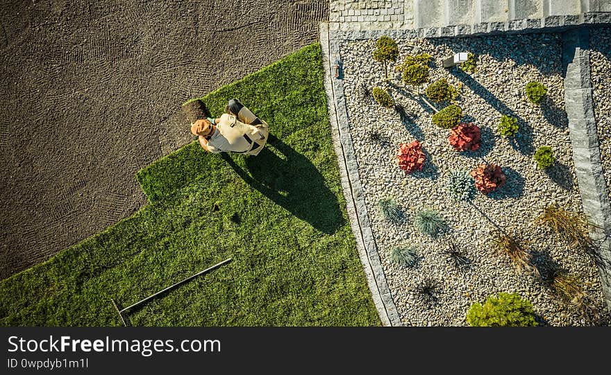 Landscaping and Gardening. Aerial View of Gardener Installing Brand New Grass in Newly Developed Residential Garden. Industrial Theme