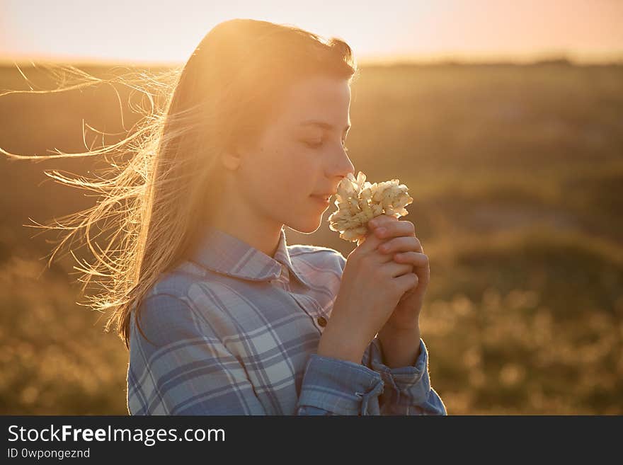 A Teenage Girl In A Field At Sunset With Flowers In Her Hands.