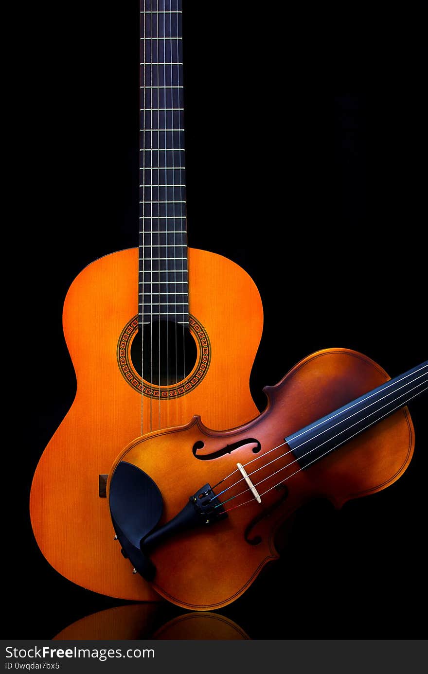 A close study of shapes and elements of design - vintage violin and wooden guitar side by side on dark backdrop. A close study of shapes and elements of design - vintage violin and wooden guitar side by side on dark backdrop.