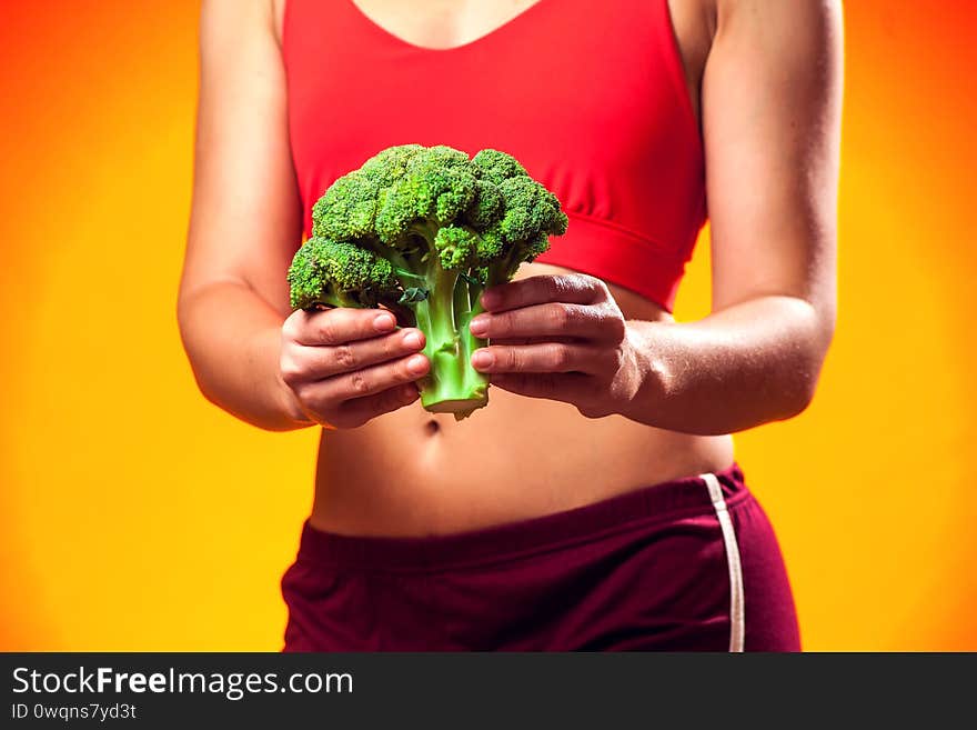 Woman in sportswear holding broccoli. People, fitness and dieting concept. Woman in sportswear holding broccoli. People, fitness and dieting concept