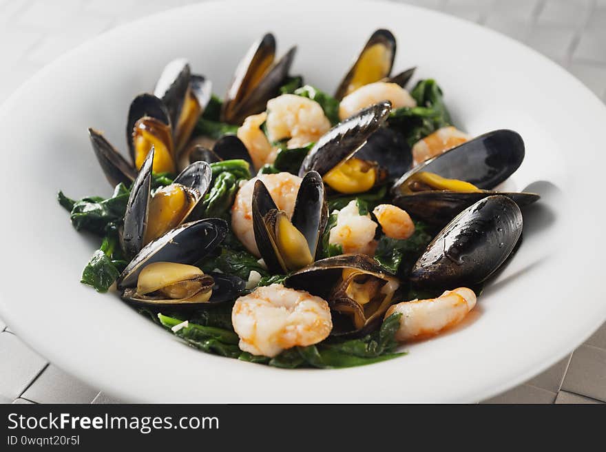 Steamed mussels with spinaches and shrimps in a soup white plate. Steamed mussels with spinaches and shrimps in a soup white plate