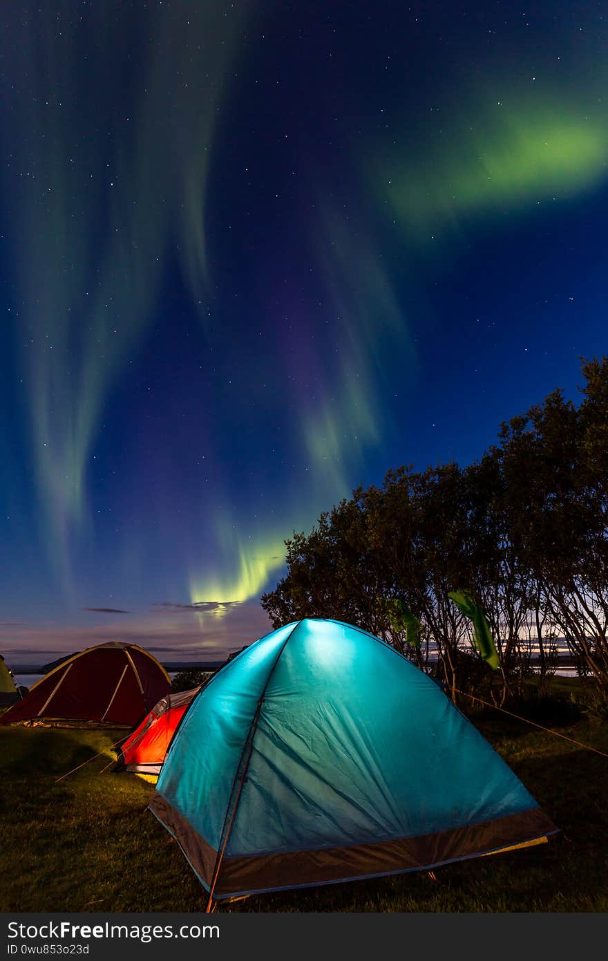Wide angle night view of a camping resort with a blue and red sleeping tents under a sky lit by northern lights. Wide angle night view of a camping resort with a blue and red sleeping tents under a sky lit by northern lights