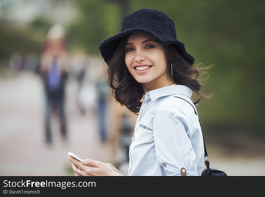 A beautiful woman close up, that is smiling for the camera, while in an urban environment, holding a mobile phone