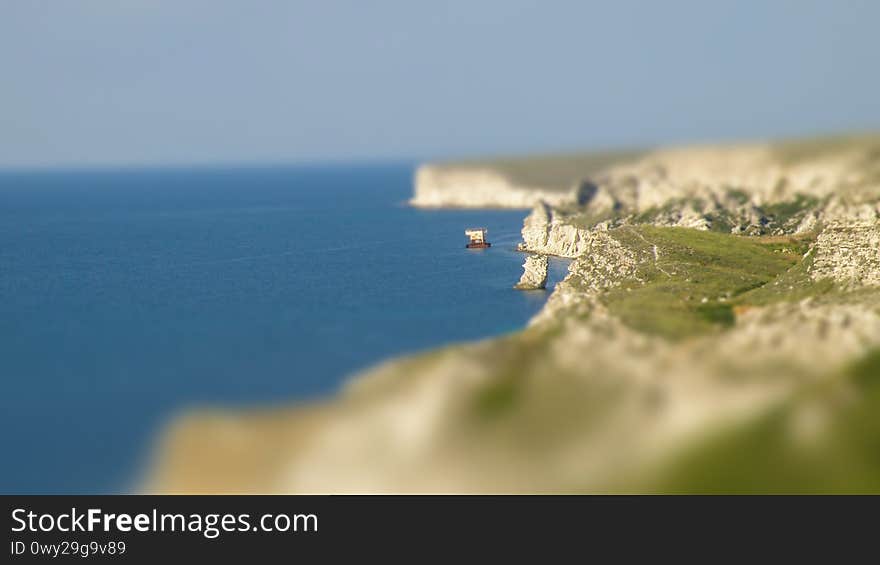 Tilt-Shift photograph of a sheer rocky seashore. View of the seashore and the old sunken ship. Rocks of white limestone. Miniature effect.