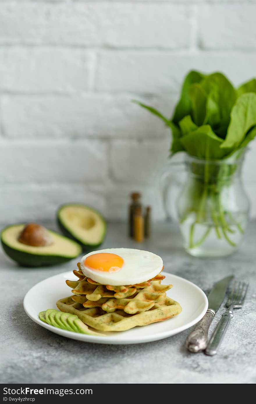 Fresh delicious and nutritious breakfast with waffles with spinach, fried egg and avocado pieces