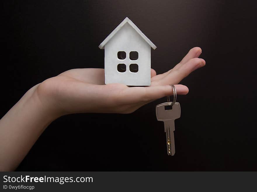 Close-up of hand holding keys and model of a white wooden house on black background. Copyspace