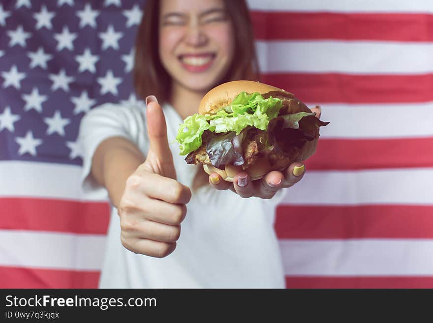 Selective focus on hamburger and thumb up with blur background of woman and american flag to celebrate Independence day on 4th of July. Selective focus on hamburger and thumb up with blur background of woman and american flag to celebrate Independence day on 4th of July