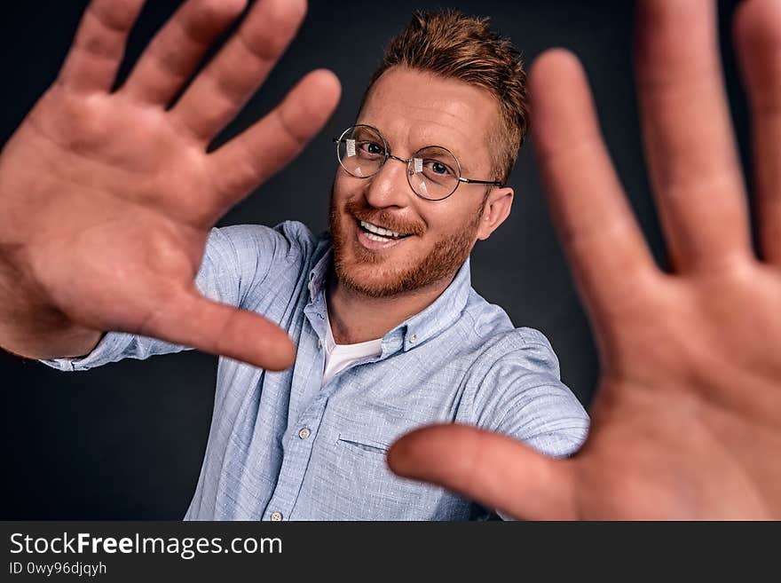 Man trying make selfie to post it online. Portrait of stylish and happy handsome yong man with thick readbeard and stylish haircut, pulling hands towards camera as if making photo of himself, smiling