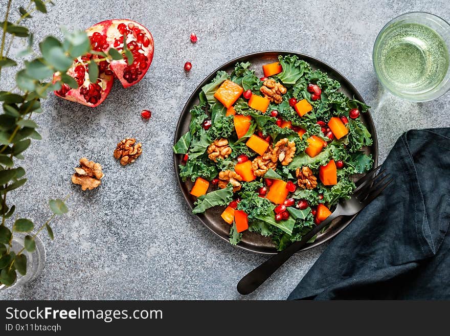 Top view on a vegan fitness salad which is made from raw vegetables such a persimmon, kale, pomegranate seeds and walnut. Healthy food and lifestyle concept, flat lay