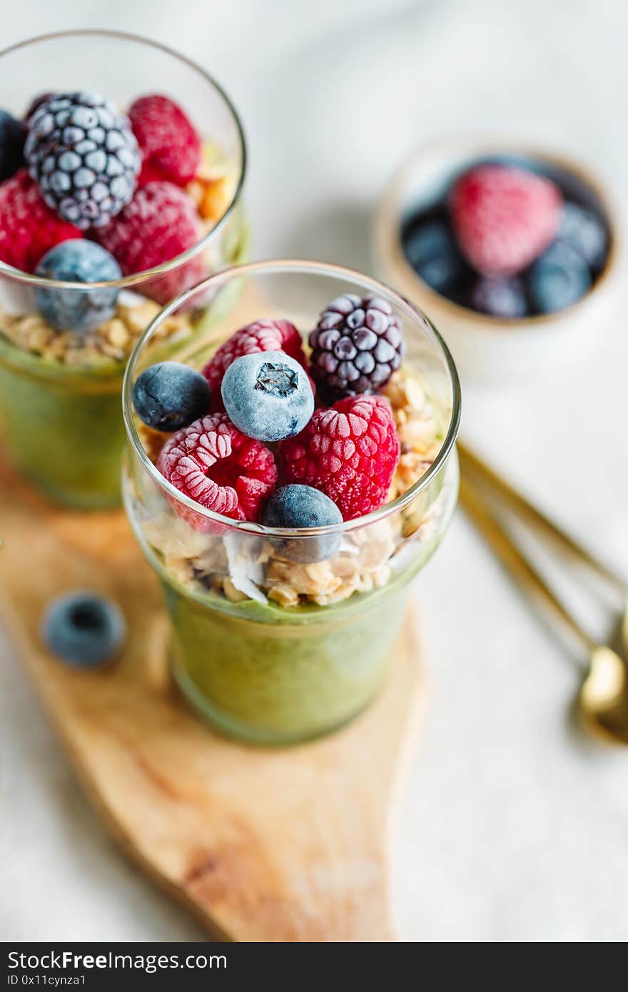 Top view on portions of chia pudding with matcha tea, organic granola, frozen berries in glasses