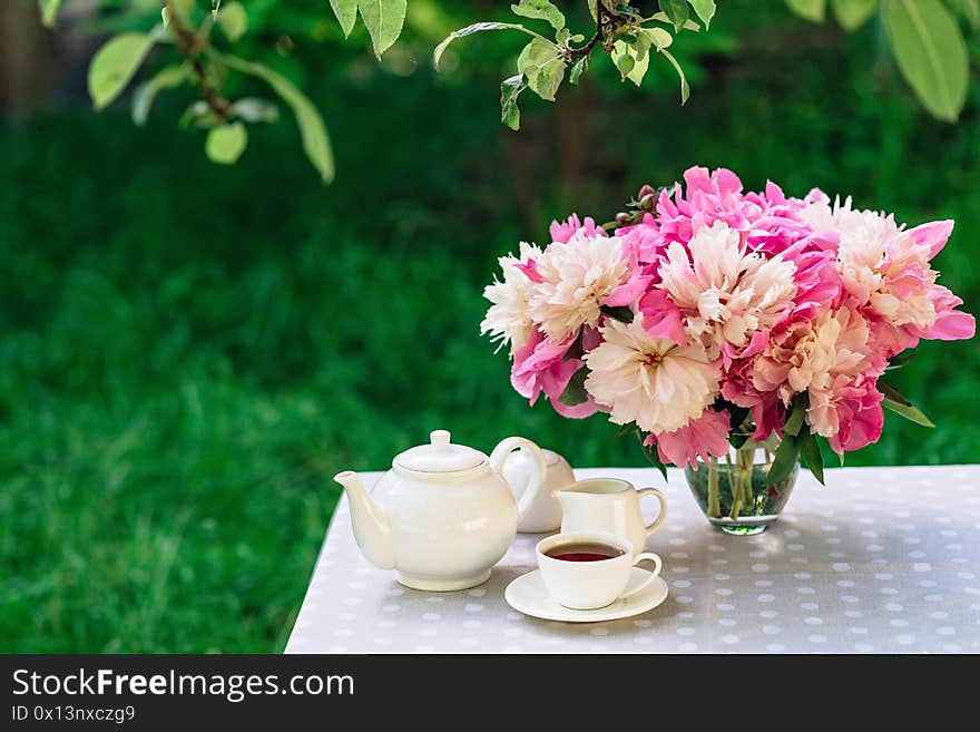 A cozy romantic breakfast in the open air. Peony flower vase, teapot and cup of tea, macaroon cake on the table. Congratulations on mother`s day or women`s day. Soft selective focus.