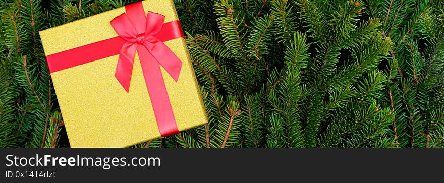 Poster. Golden gift box with a red bow on the background of fir branches. There is a place for inscription. Close up, top view.