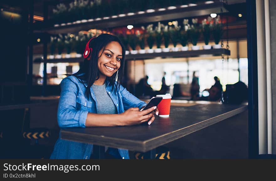 Portrait of attractive dark skinned hipster girl listening to music in headphones using application with favorite playlist. Portrait of attractive dark skinned hipster girl listening to music in headphones using application with favorite playlist.