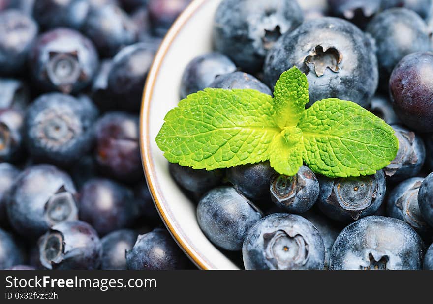 Fresh blueberries in a bowl with mint leaf background or backdrop. Vegan and vegetarian concept. Macro texture of blueberry