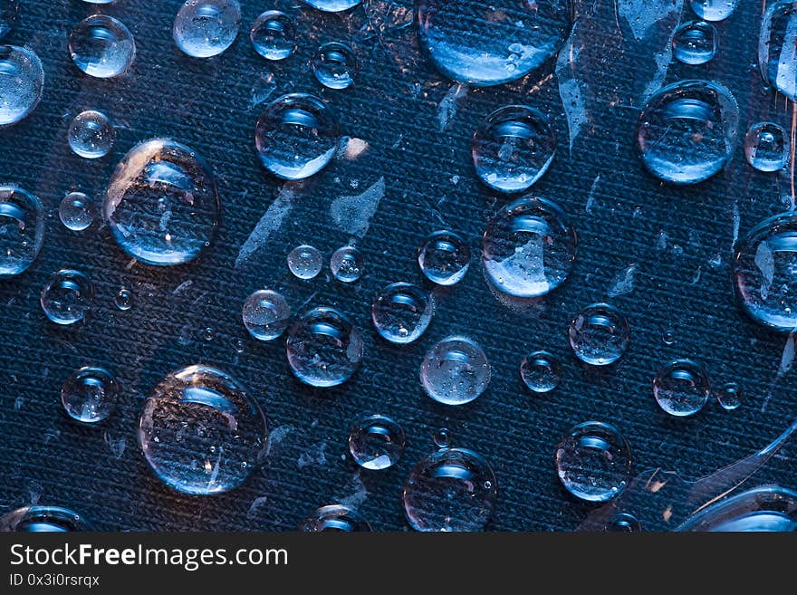 Texture. Transparent raindrops are located on the blue cloth background. Close-up.